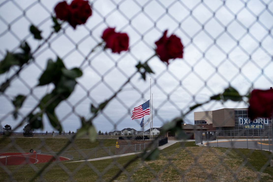 Roses hang from a fence and the American flag is lowered December 7, 2021, outside Oxford High School in Michigan to honor victims of the prior week's shooting there.