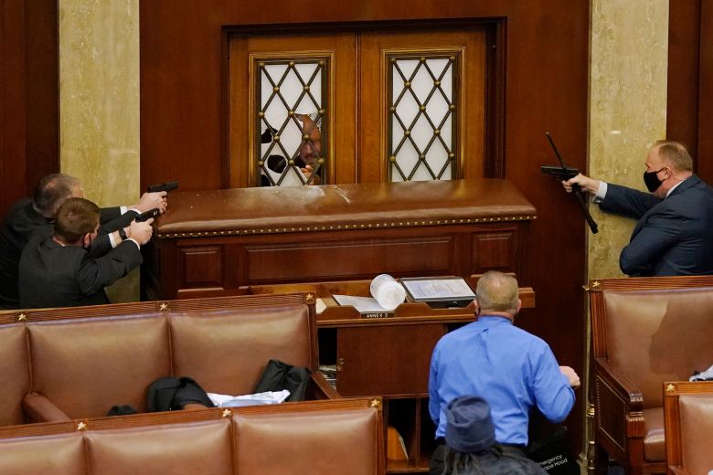 US Capitol police officers aim their weapons at the main door in the House Chamber during the January 6, 2021 insurrection at the US Capitol.