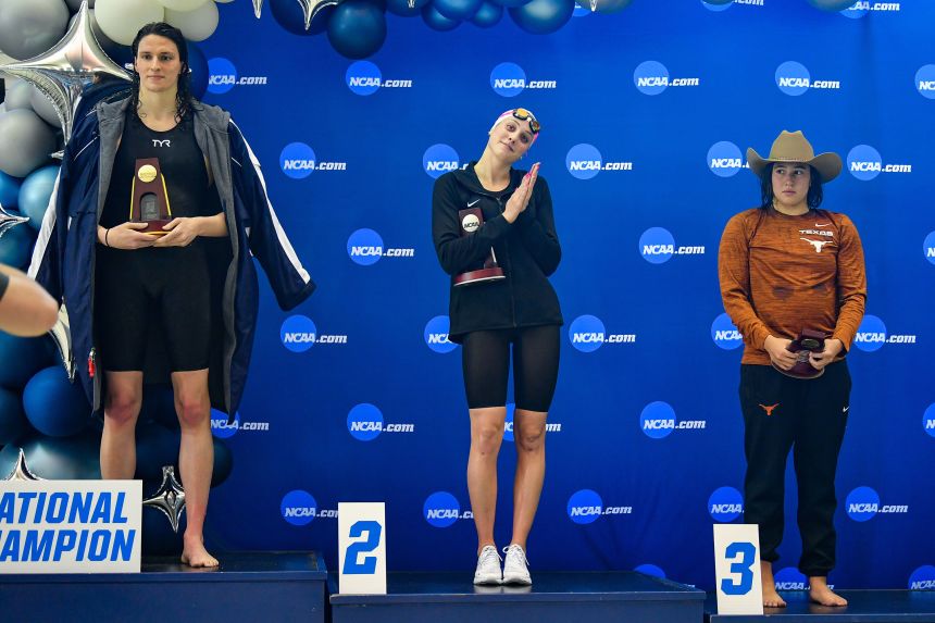 University of Pennsylvania swimmer Lia Thomas accepts the winning trophy for the 500 Freestyle finals as second-place finisher Emma Weyant and third-place finisher Erica Sullivan watch during the NCAA Swimming and Diving Championships on March 17, 2022, at the McAuley Aquatic Center in Atlanta, Georgia.
