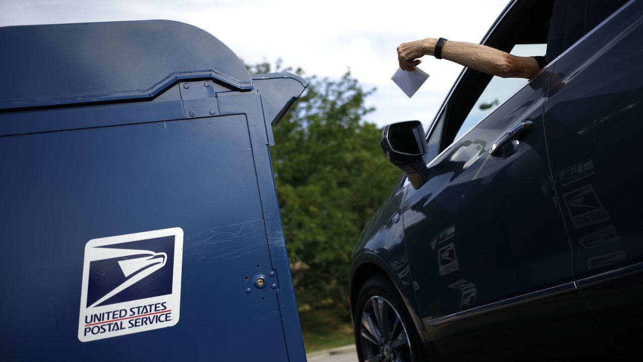 A motorist drops a letter into a United States Postal Service (USPS) mail drop box at a post office in Covington, Kentucky, US, on Saturday, July 2, 2022. Beginning July 10, the cost of postage stamps will increase from 58 cents to 60 cents, and the cost to mail one metered mail piece will increase from 53 cents to 57 cents. Photographer: Luke Sharrett/Bloomberg via Getty Images