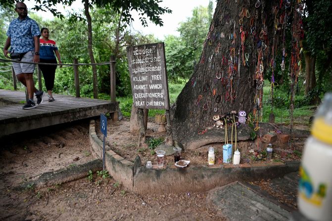 Tourists walk past a tree used to beat children to death in the former Khmer Rouge prison camp at the Choeung Ek killing fields memorial in Phnom Penh, Cambodia.