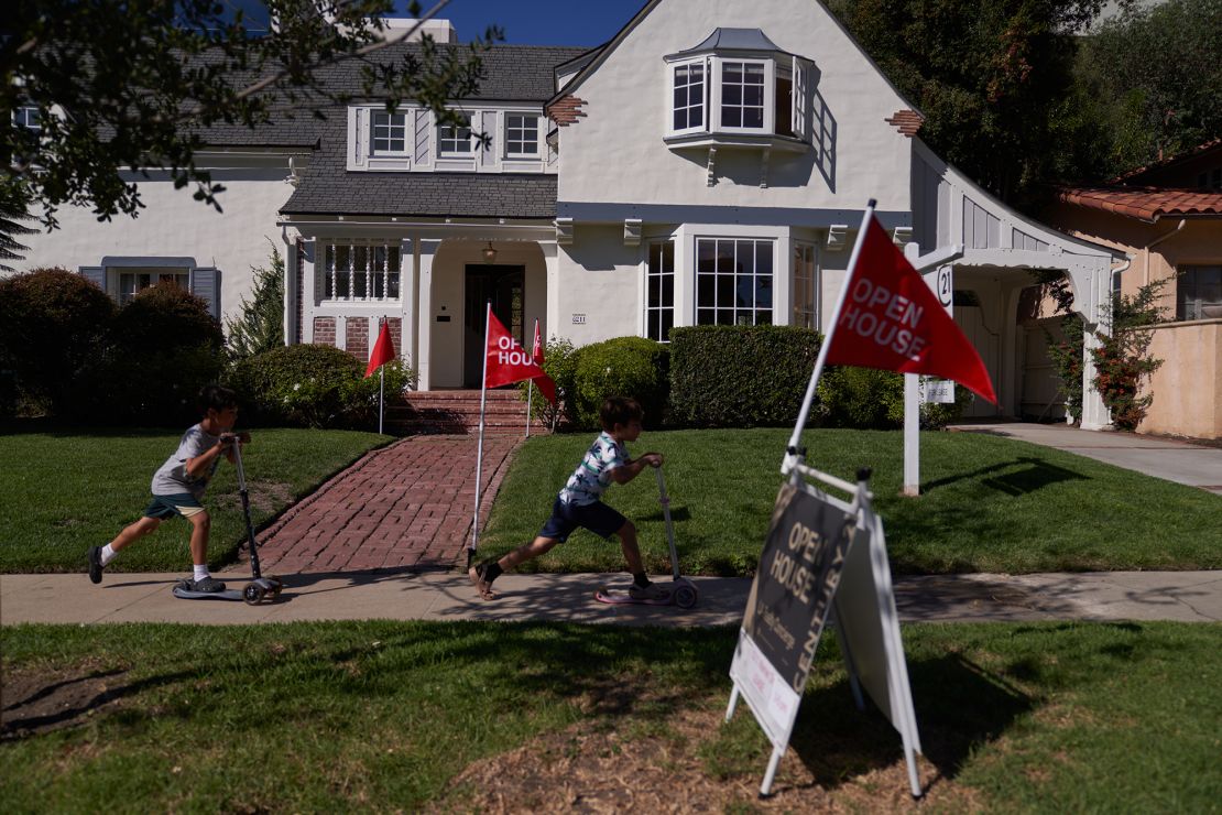 Children ride scooters past and 'open house' flags displayed outside a single family home on September 22, 2022 in Los Angeles, California.