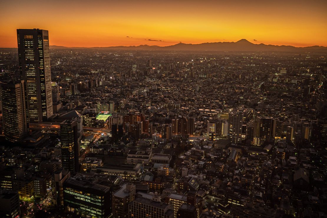 Mount Fuji is visible in the distance behind the Tokyo skyline at dusk.