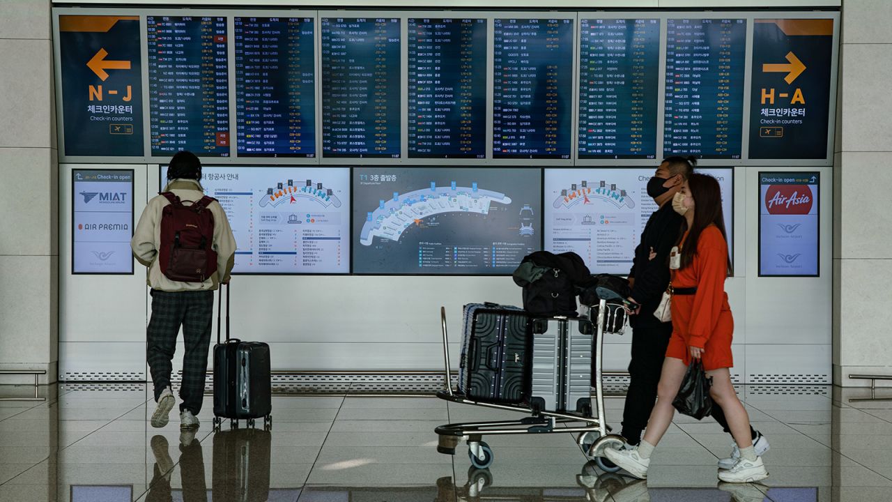 Passengers with luggages walk in front of a flight information board at Incheon International Airport on January 18, 2023, South Korea.
