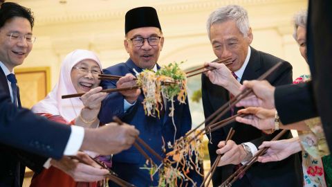 Singapore Deputy Prime Minister Lawrence Wong (L), Malaysian Prime Minister Anwar Ibrahim (3rd L) and his wife Wan Azizah (2nd L), Singapore's Prime Minister Lee Hsien Loong (2nd R) and his wife Ho Ching (R) mix a traditional Chinese lunar new year dish Yusheng during a lunch at the Istana Presidential Palace in Singapore on January 30, 2023. (Photo by HOW HWEE YOUNG / POOL / AFP) (Photo by HOW HWEE YOUNG/POOL/AFP via Getty Images)
