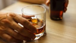 Whiskey or cognac glass with ice and bottle in a hand on a wooden background.