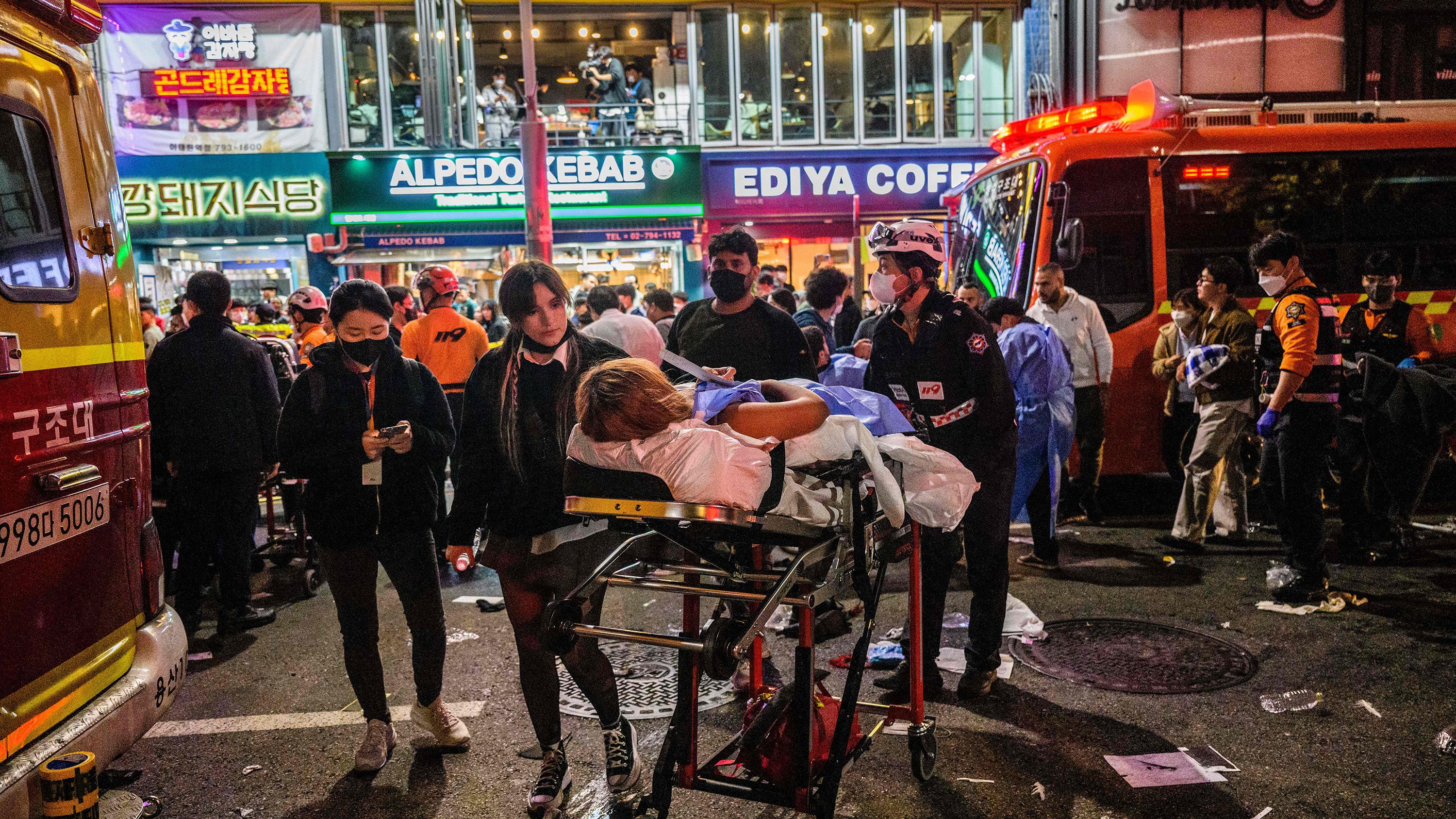 In this photo taken early on October 30, 2022, rescue workers help a person  on a stretcher after a Halloween crowd crush that took place in a nearby alleyway in the popular district of Itaewon in Seoul.
