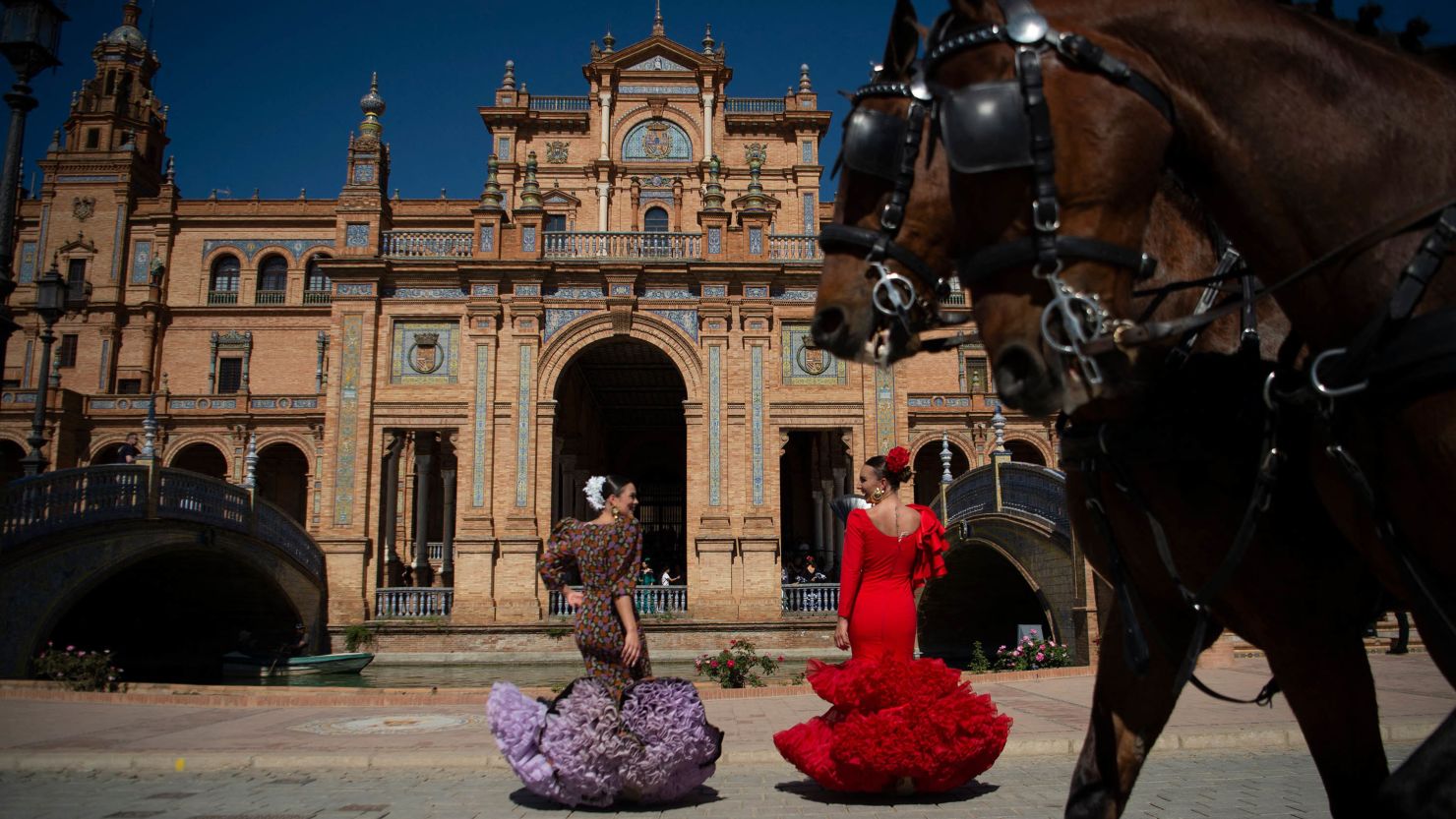 Women wearing traditional Andalusian dress stand in Seville's celebrated Plaza de Espana.