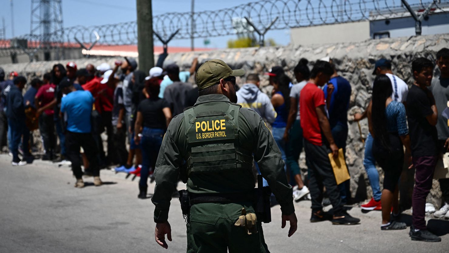 A Border Patrol agent walks along a line of migrants waiting to turn themselves in to US Customs and Border Protection after crossing the US-Mexico border in El Paso, Texas on May 9, 2023.