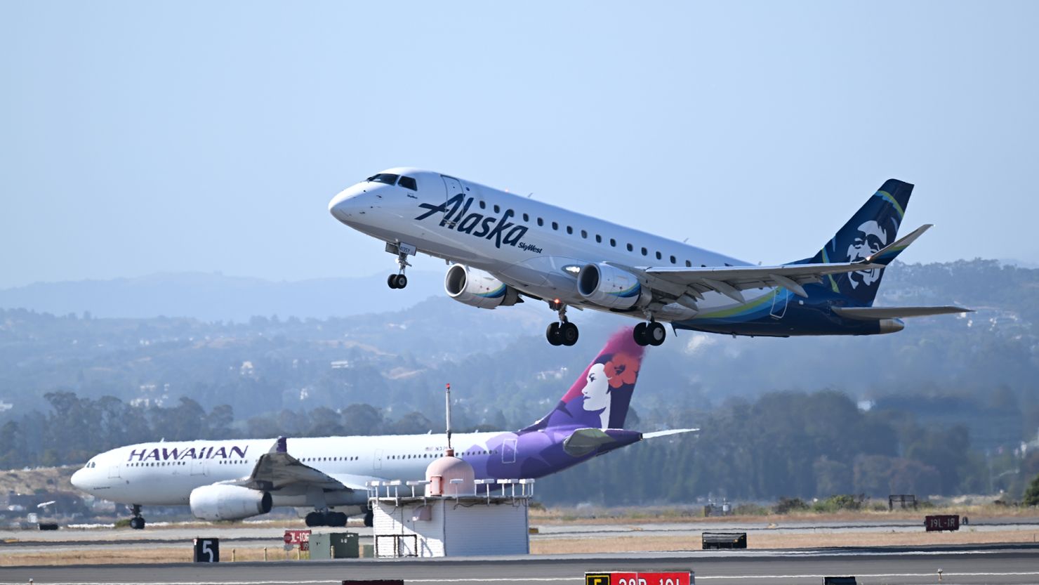 Alaska and Hawaiian Airlines planes takeoff at the same time from San Francisco International Airport on June 21, 2023. Alaska's proposed merger with Hawaiian has received Justice Department clearance.