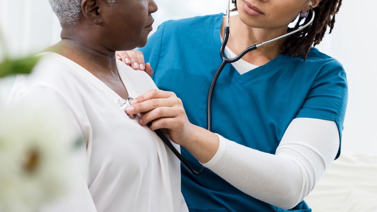 A caring mid adult female home healthcare nurse uses a stethoscope to check the heart and lungs on a senior female patient.
