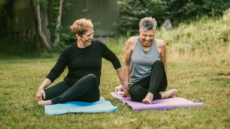 Smiling woman assisting friend while exercising on mat in public park