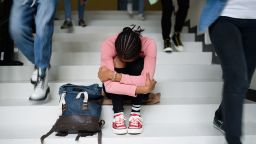 Depressed young student with face mask sitting and studying on floor back at college or university, coronavirus concept.