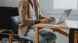 Telecommuting: unrecognizable man sitting at the desk of his home office and doing work on his laptop PC