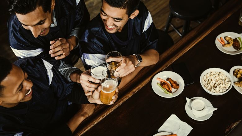 High angle view of excited sports fans toasting beer glasses at counter in bar