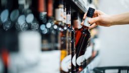Close up of woman walking through liquor aisle and choosing a bottle of liquor from the shelf in a supermarket