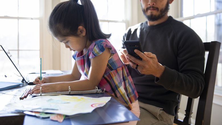 Father working from home and helping daughter with schoolwork