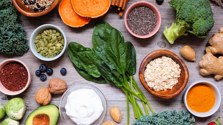 Group of healthy food ingredients. Overhead view table scene on a wooden background. Super food concept with green vegetables, berries, whole grains, seeds, spices and nutritious items.