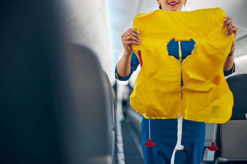 Close up portrait of young beautiful flight attendant holding life jacket in hands while demonstrating how using it