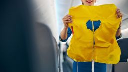 Close up portrait of young beautiful flight attendant holding life jacket in hands while demonstrating how using it