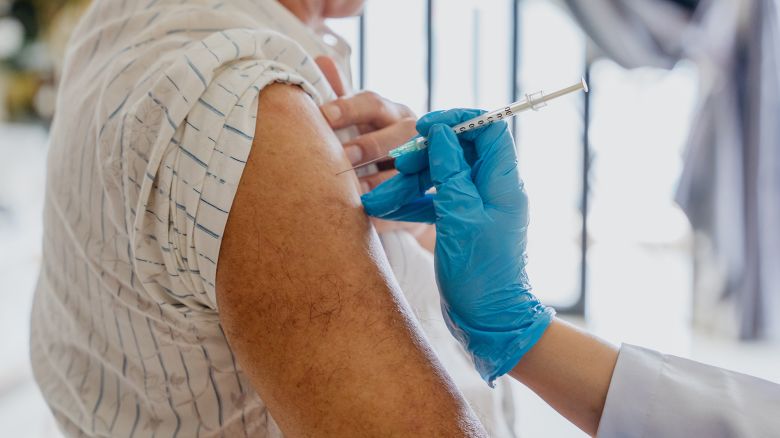 Close up image of an Asian senior man getting a vaccine injection on his arm from a doctor