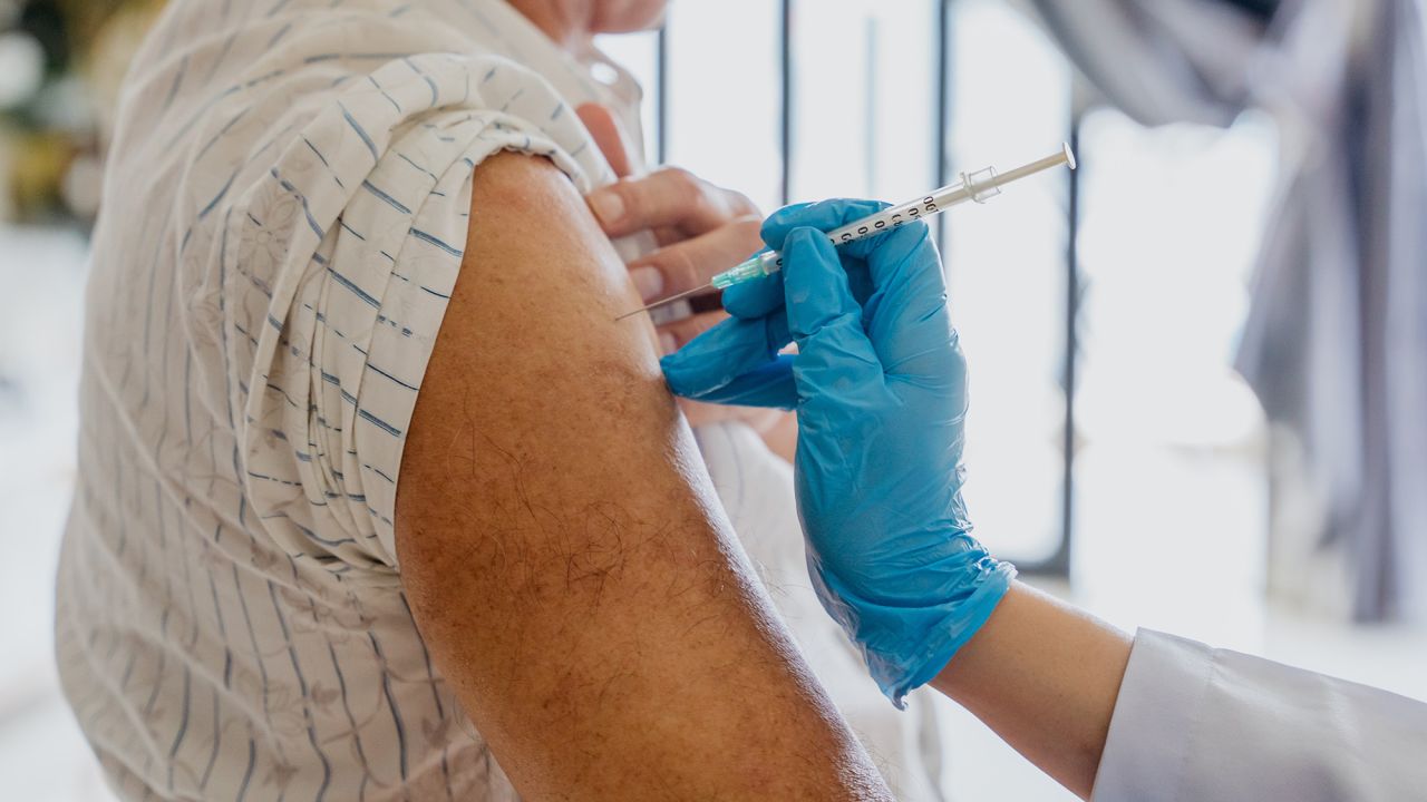 Close up image of an Asian senior man getting a vaccine injection on his arm from a doctor