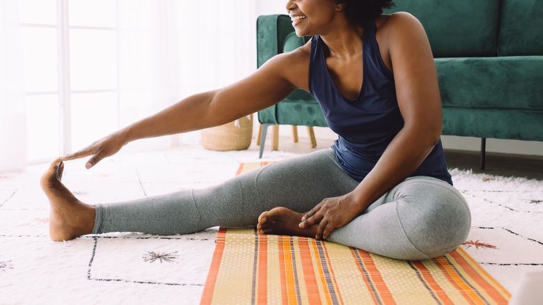 African woman doing exercise at home. Mature woman doing stretching workout in living room.