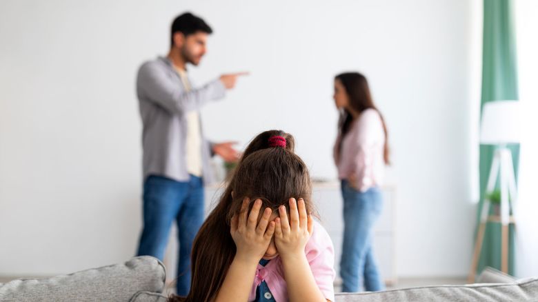 Family crisis. Little girl crying, closing face with hands while her angry parents fighting on the background, depressed child feeling lonely, selective focus