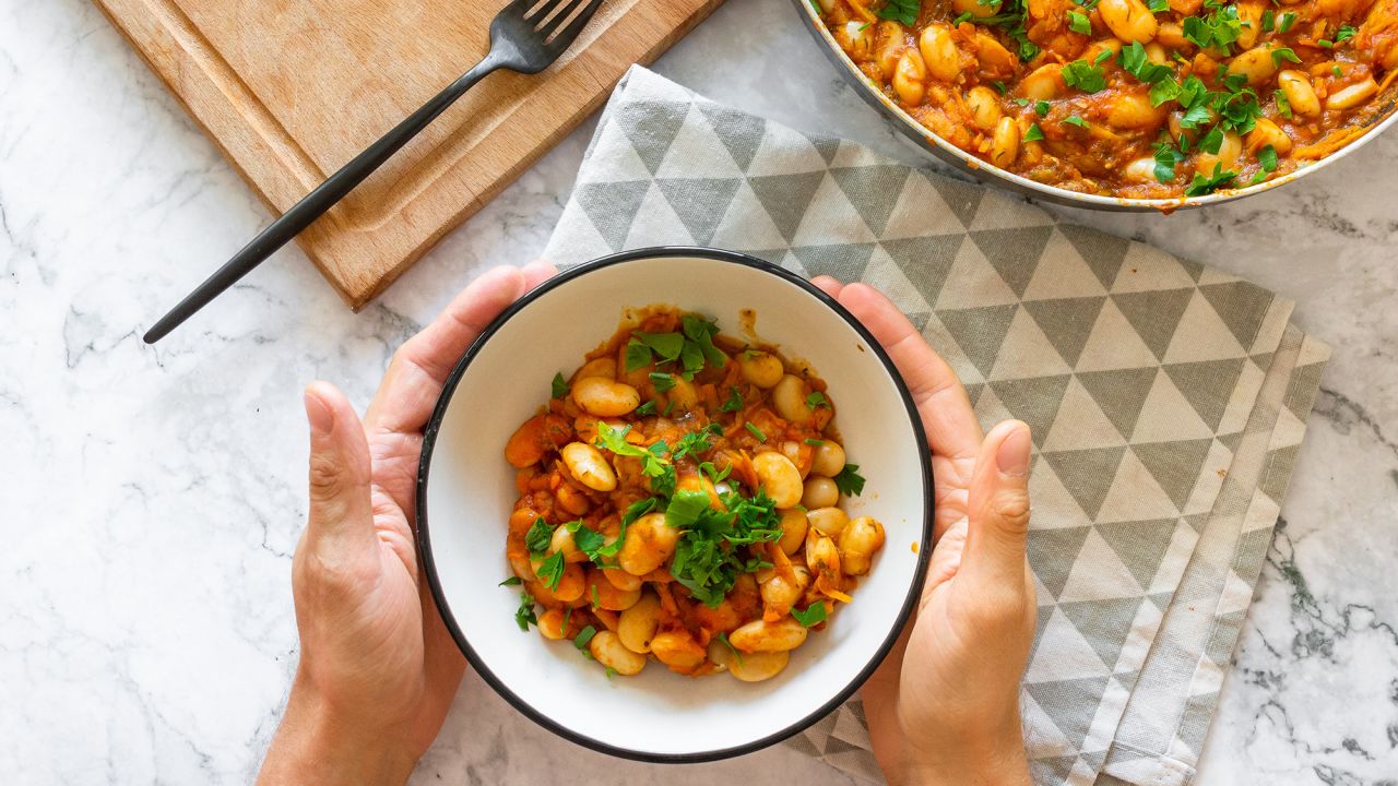 Tomato lobio of white bean pods and herbs in a bowl on a marble background. Lenten dish. Flat lay, top view thaditional georgian dish