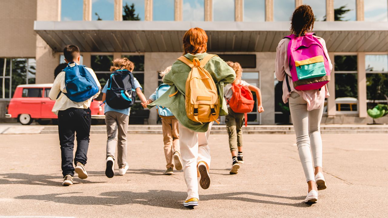 Little kids schoolchildren pupils students running hurrying to the school building for classes lessons from to the school bus. Welcome back to school. The new academic semester year start