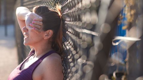 Waist-up view of an exhausted woman leaning against a wire fence.