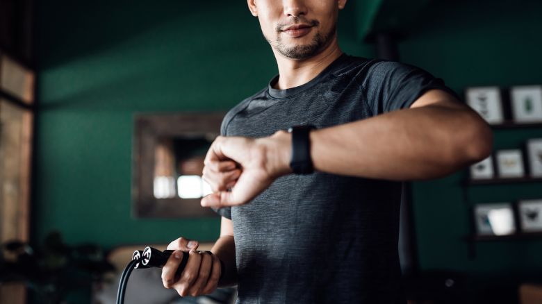 Active young Asian man exercising at home, using fitness tracker app on smartwatch to monitor training progress and measuring pulse. Keeping fit and staying healthy. Health, fitness and technology concept