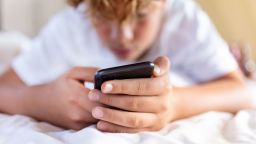Teenager boy is using smartphone at home in bed - stock photo
