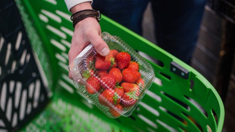 Male hand puts plastic box with strawberries in store basket