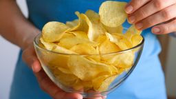 The girl takes crispy fried fatty potato chips from a glass bowl or plate, on a white background or table. Chips in the hands of a woman, she eats them. The concept of an unhealthy diet and lifestyle, the accumulation of excess weight.