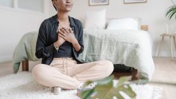 Woman with hand on chest showing gratitude while praying sitting on the floor in her bedroom. Spirituality concept.