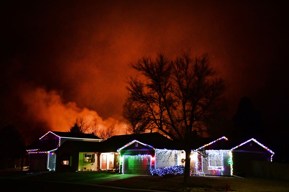Christmas lights adorn a house as the Marshall Fire rages in the background on December 30, 2021, in Louisville, Colorado.