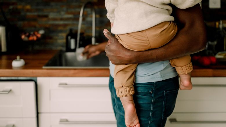 Midsection of father carrying baby boy while doing chores in kitchen