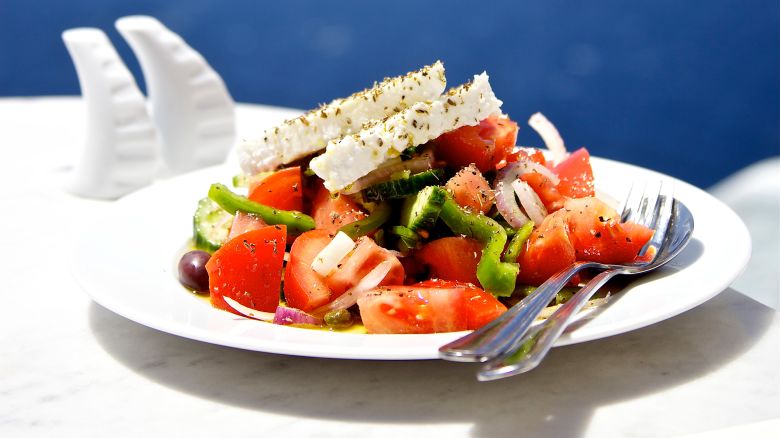 Greek salad on white plate in front of sea.