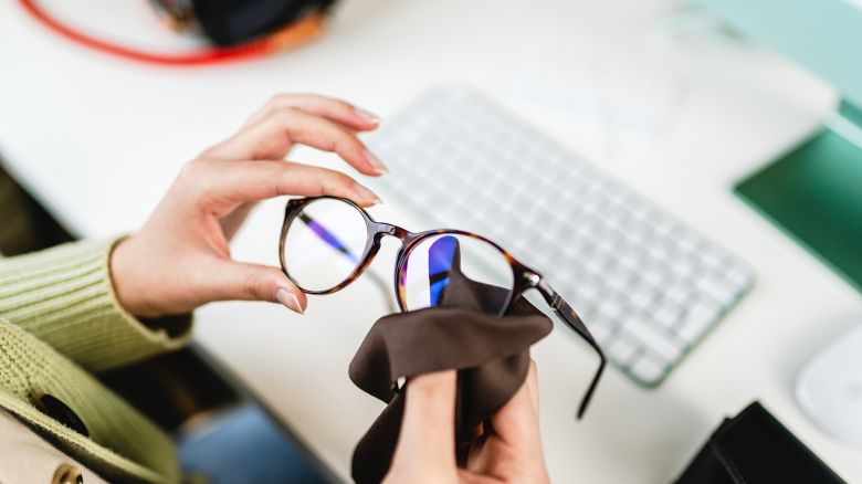 Unrecognizable female hand wiping glasses in office