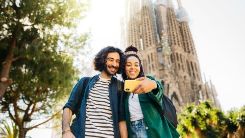 Smiling couple taking selfie through mobile phone while standing against Sagrada Familia at Barcelona, Catalonia, Spain