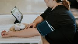 Asian woman checking her blood pressure while having virtual appointment with her doctor.