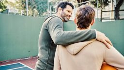 Father and son walking after playing a game of basketball. Young man and teenage boy having fun, talking and chatting while staying fit, active