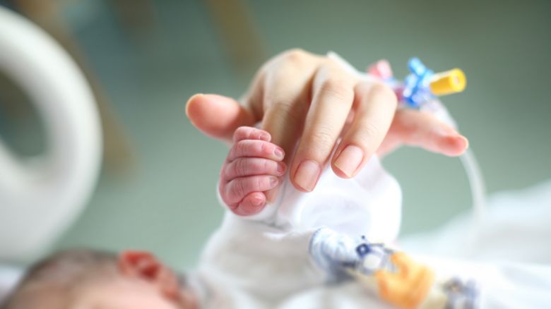 Newborn holding his mother's finger catheter on it.