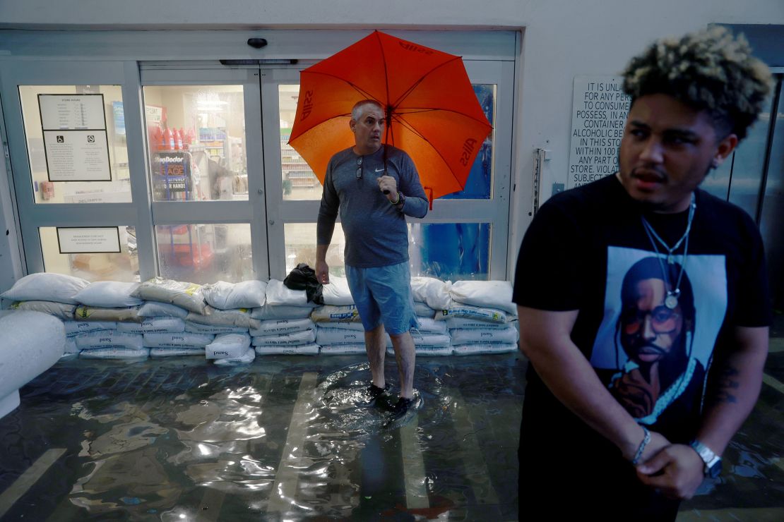 Pedestrians stand at the inundated entryway of a Publix supermarket as a deluge of rain from a tropical storm in 2022 caused flooding in Miami.