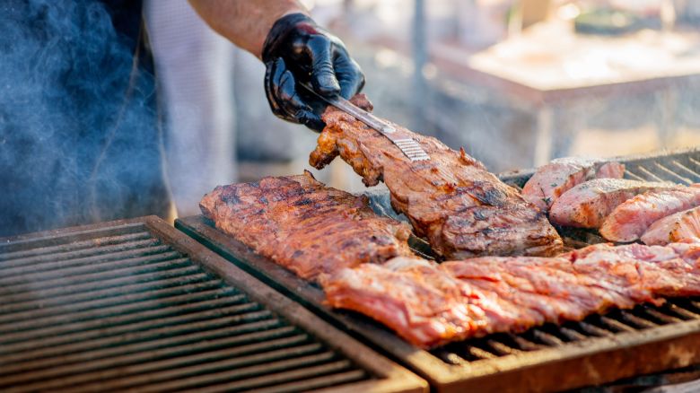 Barbecue ribs. Man in gloves flips grilled ribs on a charcoal grill. Picnic in the backyard during a family holiday. BBQ meat. 