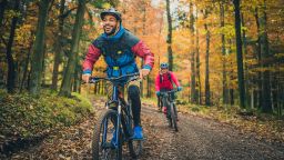 Smiling young adult black man enjoying sport with friends in nature. Adventure trip in colourful autumn forest, active lifestyle concept.
