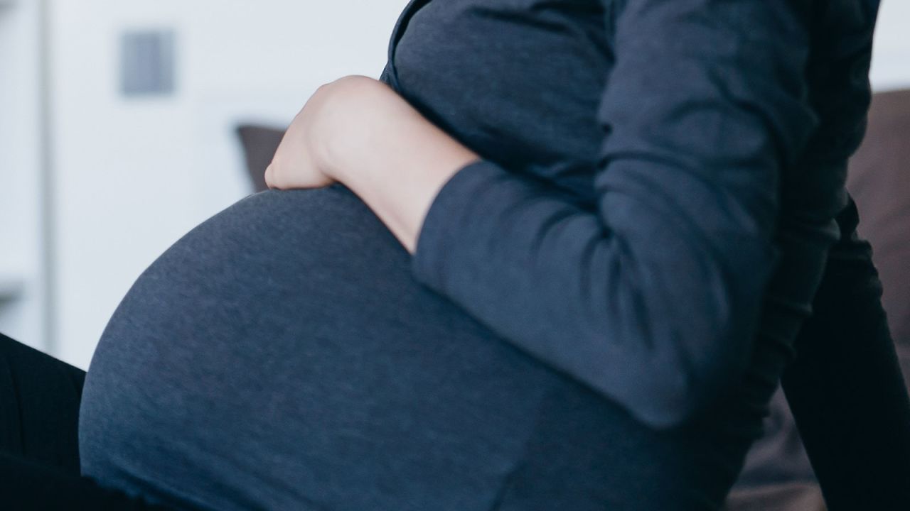 Relaxed young Asian pregnant woman with eyes closed lying on bed and listening to music over headphones. Prenatal music stimulation. Encourages the stimulation of brain development and maturation of her baby. Pregnancy health and wellness with technology