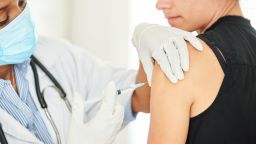 戴着防护口罩和手套的女医生在诊所给妇女接种covid-19加强剂量疫苗