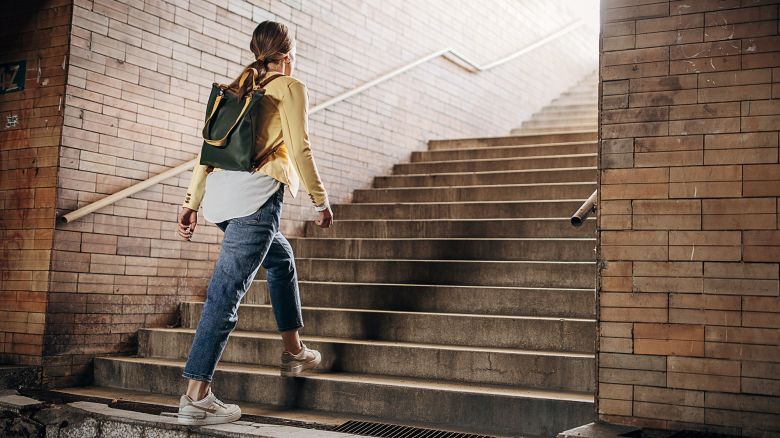 One woman, modern young woman with leather backpack moving up the steps in the underground pedestrian crossing in city.